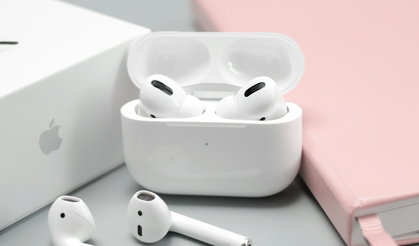Wireless earbuds in an open case beside a laptop and notebook