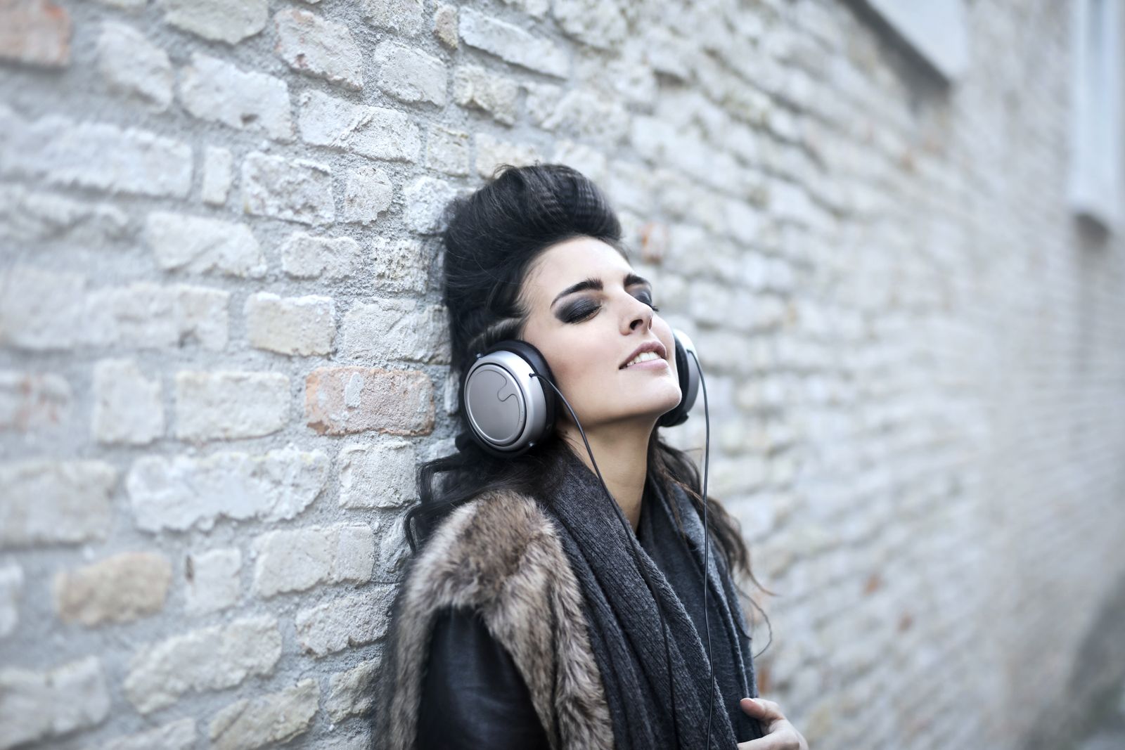 A woman wearing over-ear headphones beside an outdoor brick wall