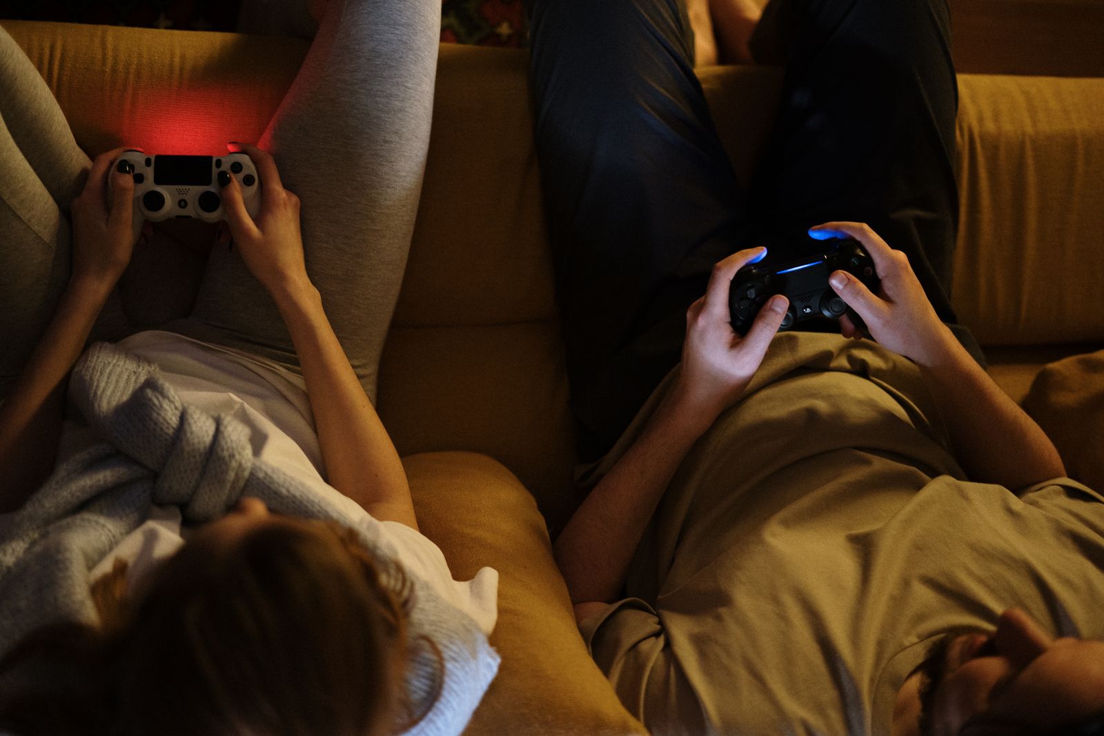 Two people holding game controllers while relaxing on a sofa