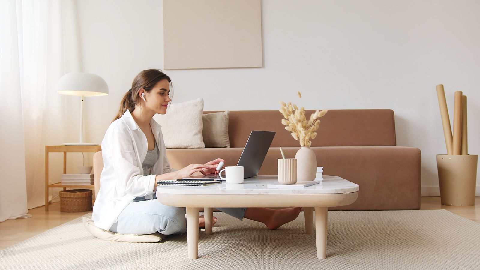 A woman working on a laptop at a low table in a living room